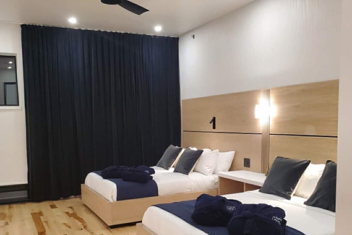 A hotel room with two beds, a ceiling fan, a nightstand, and a large window with curtains.