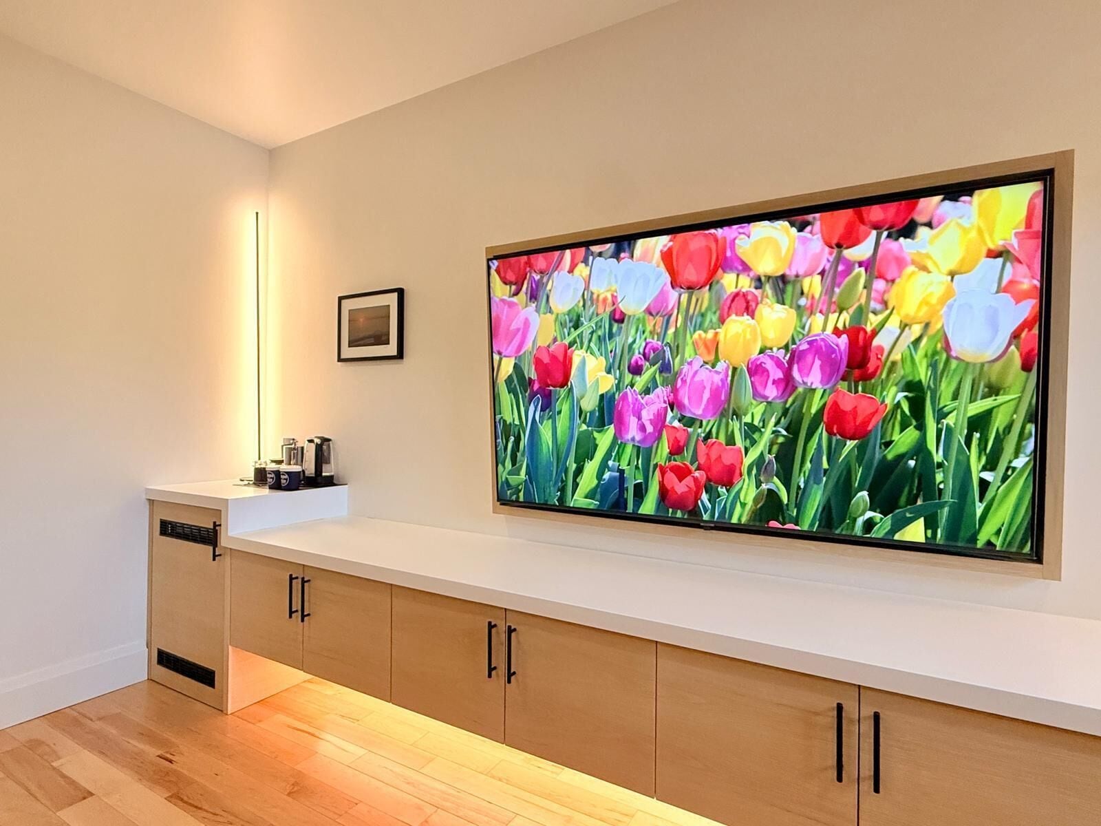 A modern living room with a large flat-screen TV mounted on the wall displaying a vibrant tulip garden.