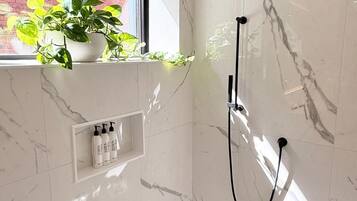 Une salle de bain moderne avec une douche, une fenêtre donnant sur un mur de briques et une étagère contenant des articles de toilette.