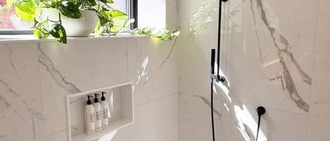Een moderne badkamer met een douche, een raam met uitzicht op een bakstenen muur en een plank met toiletartikelen.