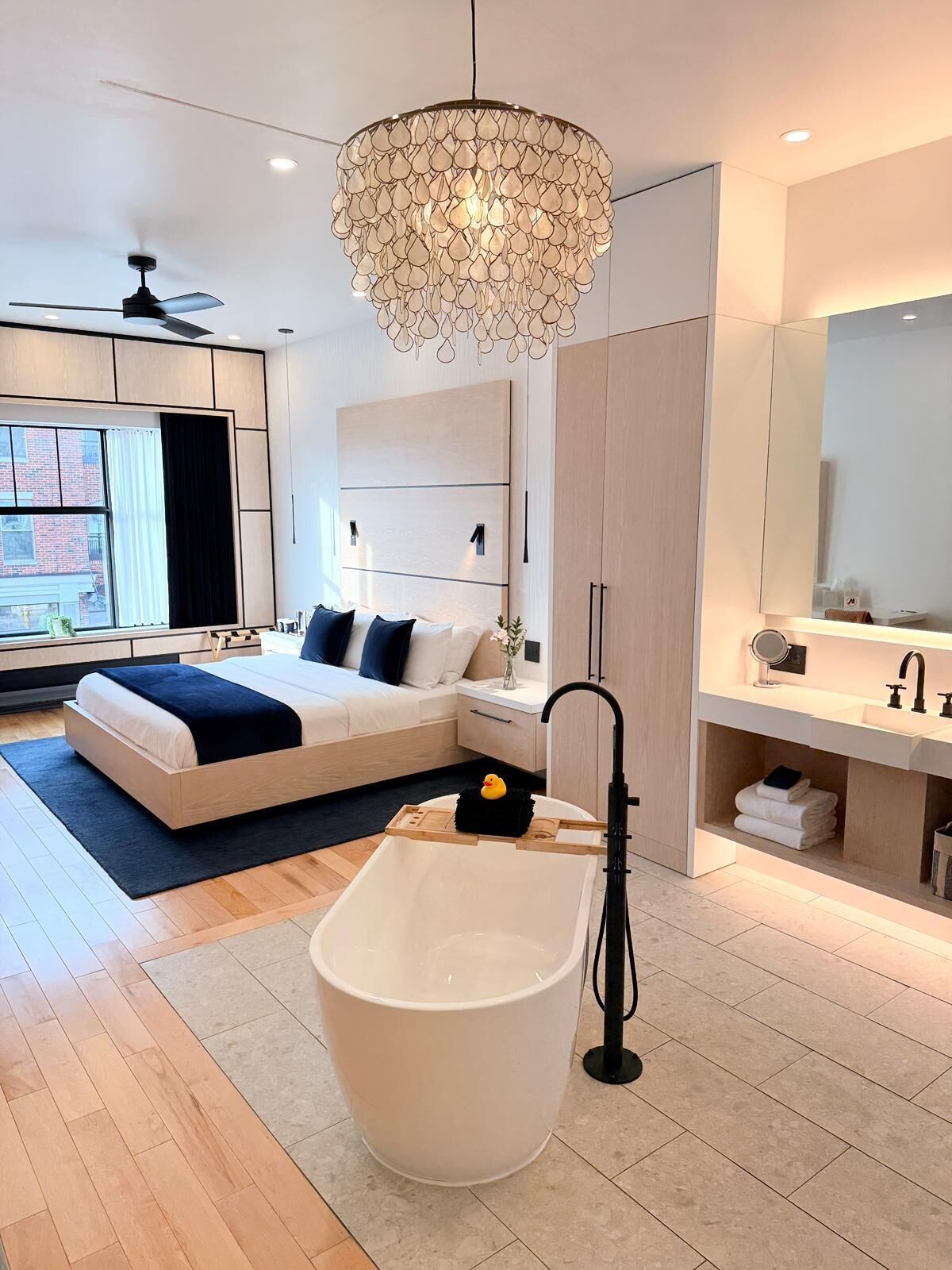 A modern bathroom with a freestanding bathtub, a large mirror, and a contemporary chandelier.