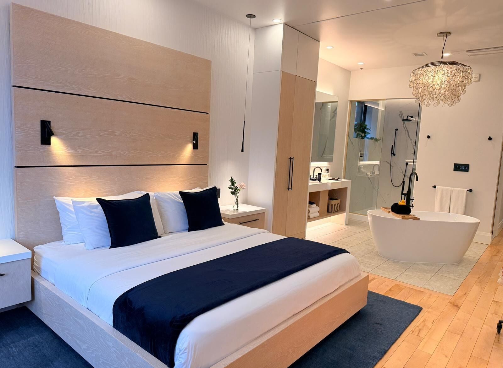 Une chambre moderne avec un grand lit, des tables de chevet, une commode, une armoire intégrée, une salle de bain avec baignoire et un lustre.