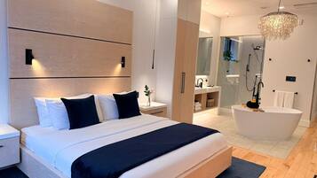 Une chambre moderne avec un grand lit, des tables de chevet, une commode, une armoire intégrée, une salle de bain avec baignoire et un lustre.