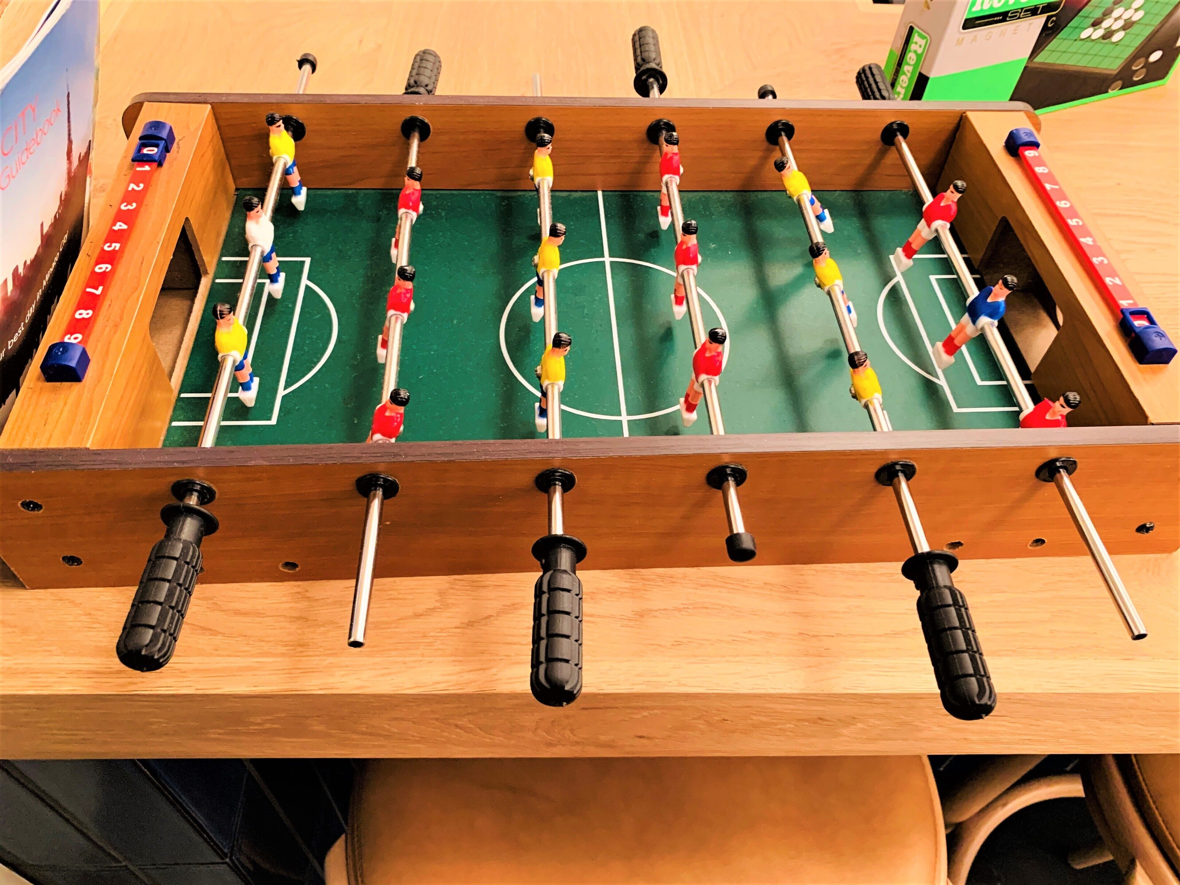 A wooden foosball table with a green playing surface and numbered scoring slots.