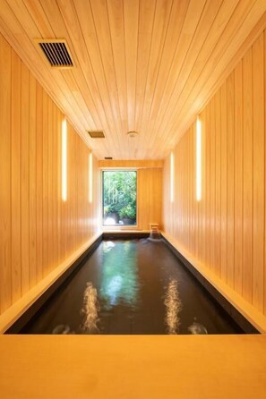 A wooden interior with a central water feature and a view of greenery outside.
