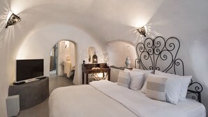 A bedroom with a curved ceiling, a bed with white bedding, a TV on a stand, and a decorative wall lamp.