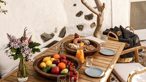 An outdoor dining area with a wooden table set for two, surrounded by stone walls and a tree.