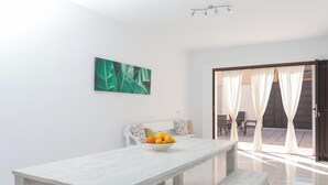 A modern dining area with a white table and bench, a bowl of fruit, and a green leaf-patterned painting on the wall. - Son Siurana - Newtly built town house with pool in Ariany (Ariany)