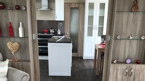 A modern interior with a central island kitchen, wooden cabinetry, and a cozy seating area. - Brand new luxury holiday home in one of the best holiday parks in the country. (Perranporth)