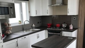 A modern kitchen with white cabinetry, a central island, a microwave, a stove, and a sink. - Brand new luxury holiday home in one of the best holiday parks in the country. (Perranporth)