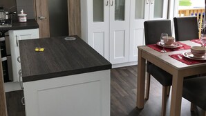 A compact kitchen with white cabinets, a black countertop, and a dining area with a table set for two. - Brand new luxury holiday home in one of the best holiday parks in the country. (Perranporth)