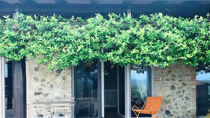 A covered patio area with a stone wall, a sliding glass door, a folding table with chairs, and an orange chair. - Colline Toscane, beautiful two-room apartment for 2/4 people, lovely view and swimming pool (Casole d’elsa, siena)