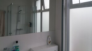 Ein Badezimmer mit Duschkabine aus Glas, einem weißen Waschbecken und einem Spiegel.
