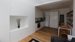 Eine moderne Küche mit weißen Schränken, ein Essbereich mit Holztisch und -stühlen sowie ein Wohnzimmer mit einer Couch.