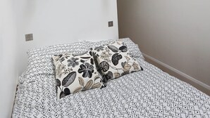 Ein Schlafzimmer mit einem Bett, gemusterten Betttextilien und einer weißen Wand.