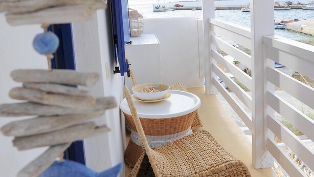 Un balcón con vista al mar, una silla de mimbre y un tapete tejido.
