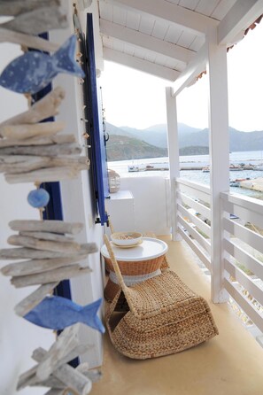 Un balcón con vista al mar, una silla de mimbre y un tapete tejido.