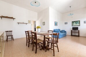 A spacious living room with a dining area, a blue sofa, a television, and a painting on the wall.