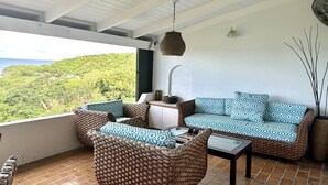 Een balkon met rieten meubilair, uitzicht op een groen landschap en een hanglamp.