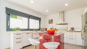 A modern kitchen with white cabinets, a red island, two white bar stools, a window with blinds, and a stainless steel range hood. - MARTE - Chalet with terrace in Sa Pobla. Free WiFi (Sa Pobla)