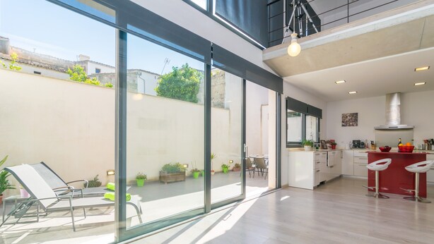 A modern kitchen with a red island, a dining area with chairs, and a large sliding glass door leading to a patio with a lounge chair and potted plants. - MARTE - Chalet with terrace in Sa Pobla. Free WiFi (Sa Pobla)