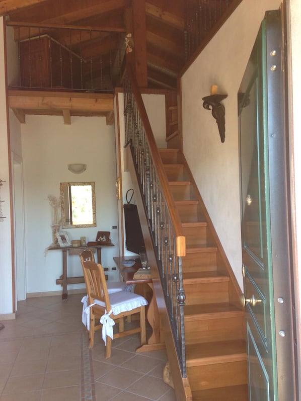 A wooden staircase with a glass door, a dining area with a table and chairs, and a wall-mounted light fixture.