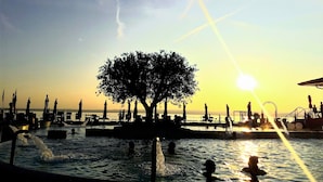 A sunset view at a waterfront with a tree in the center, water features, and a dock area. - Bed & Breakfast Le Reve (Sirmione)