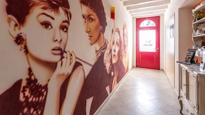A hallway with a mural of women, a red door, and a cabinet with items on it. - Bed & Breakfast Le Reve (Sirmione)