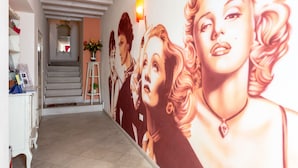A hallway with a staircase, a wall with a large mural, and a white cabinet with items on it. - Bed & Breakfast Le Reve (Sirmione)