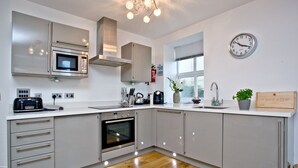 A modern kitchen with stainless steel appliances, a built-in oven, and a clock on the wall. - 5 At The Beach - Beachfront, Parking, Pets welcome (Torcross)