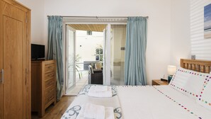 A bedroom with a bed, a wooden wardrobe, a television, and a view of the outside. - 5 At The Beach - Beachfront, Parking, Pets welcome (Torcross)