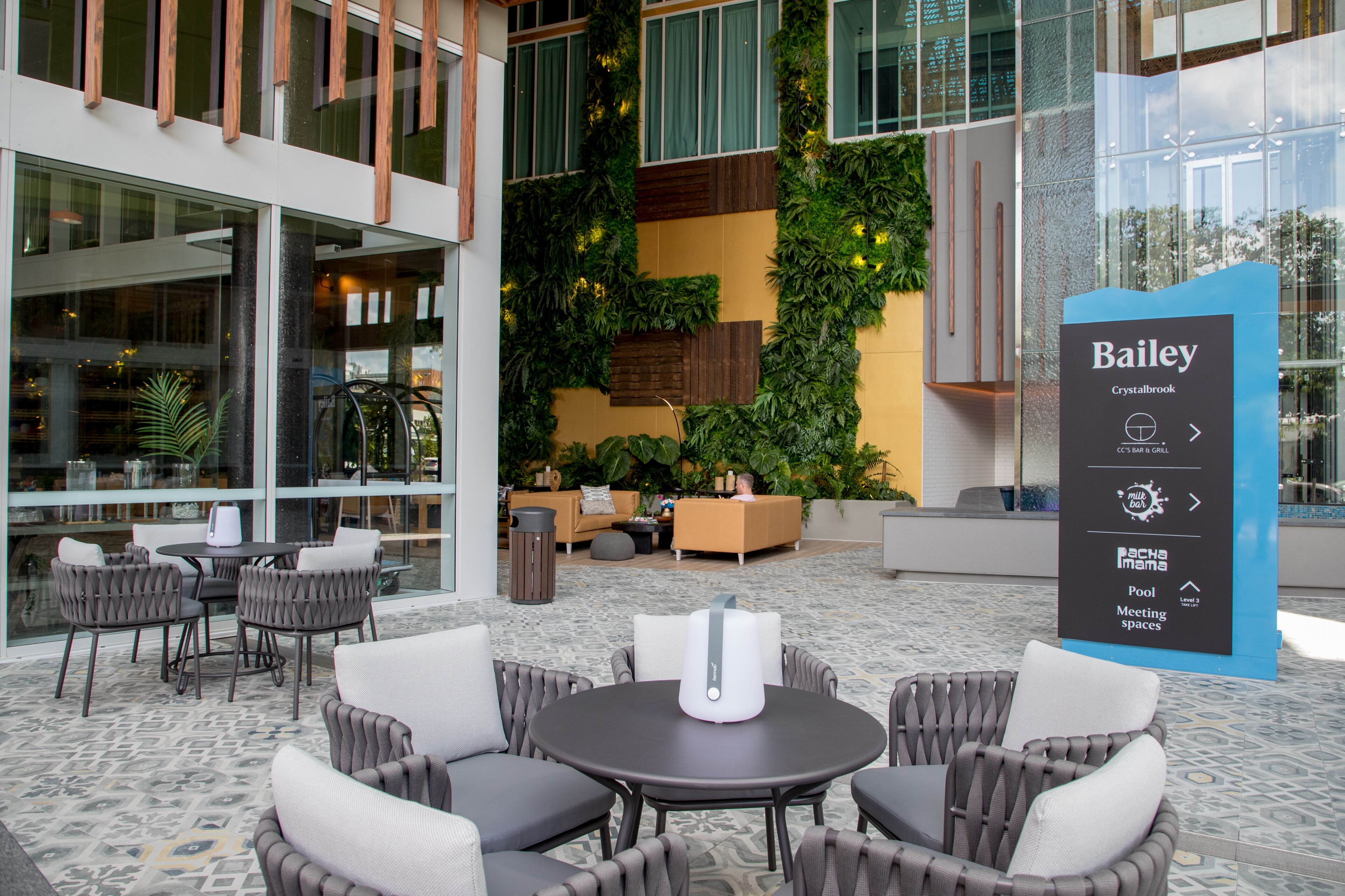 A modern outdoor seating area with wicker chairs and a round table, surrounded by lush vertical gardens and a glass wall.