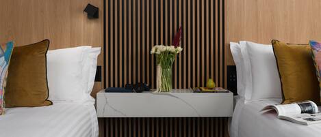 A hotel room with two beds, a wooden slat wall, a small table with a vase of flowers, a book, and a remote control.