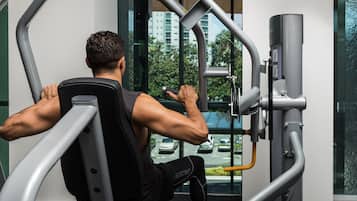 Un hombre usando una máquina de gimnasio con vista a un estacionamiento y edificios a través de una ventana.