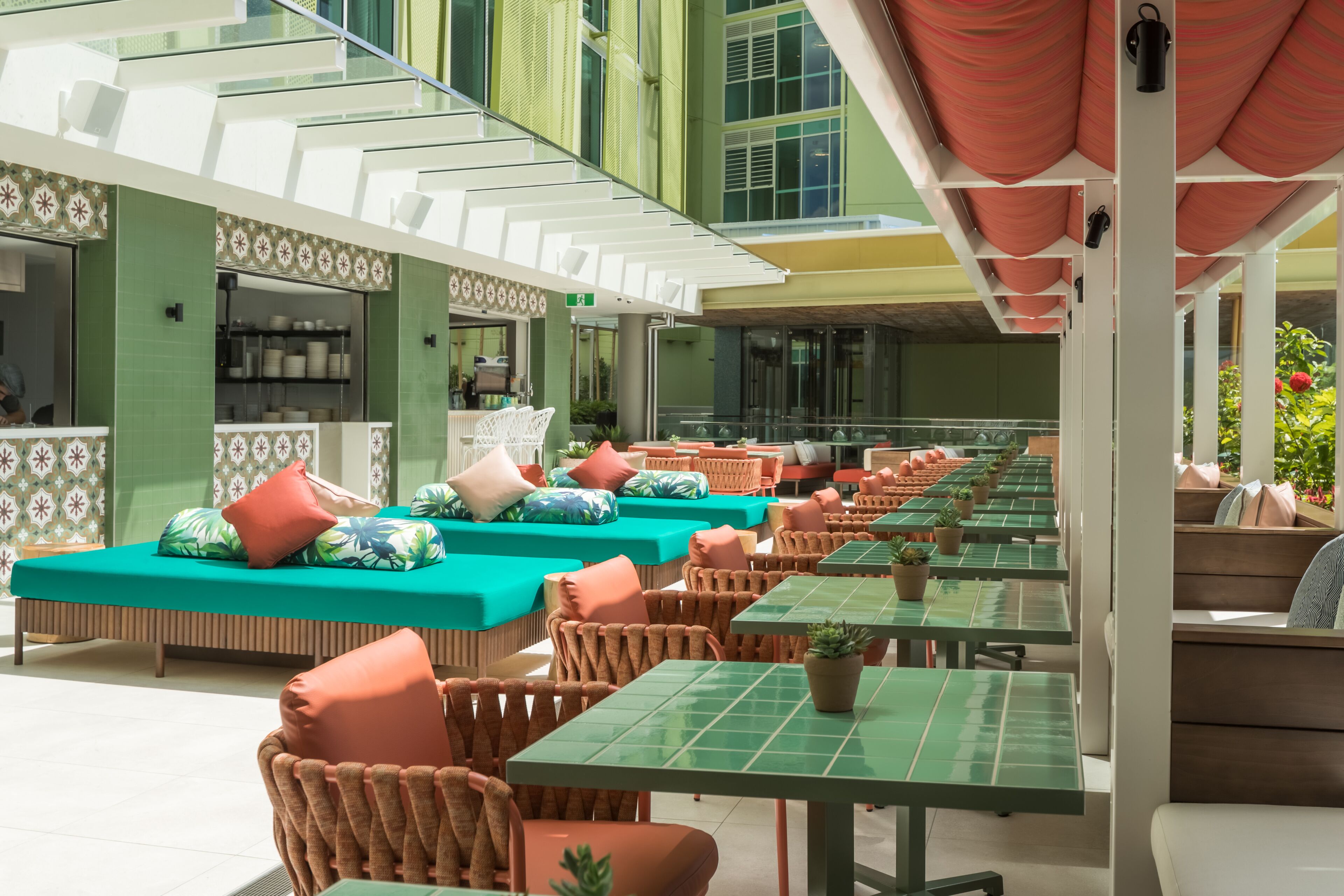 A modern outdoor seating area with green tables and wicker chairs, a kitchen area with green walls, and a staircase with white railings.