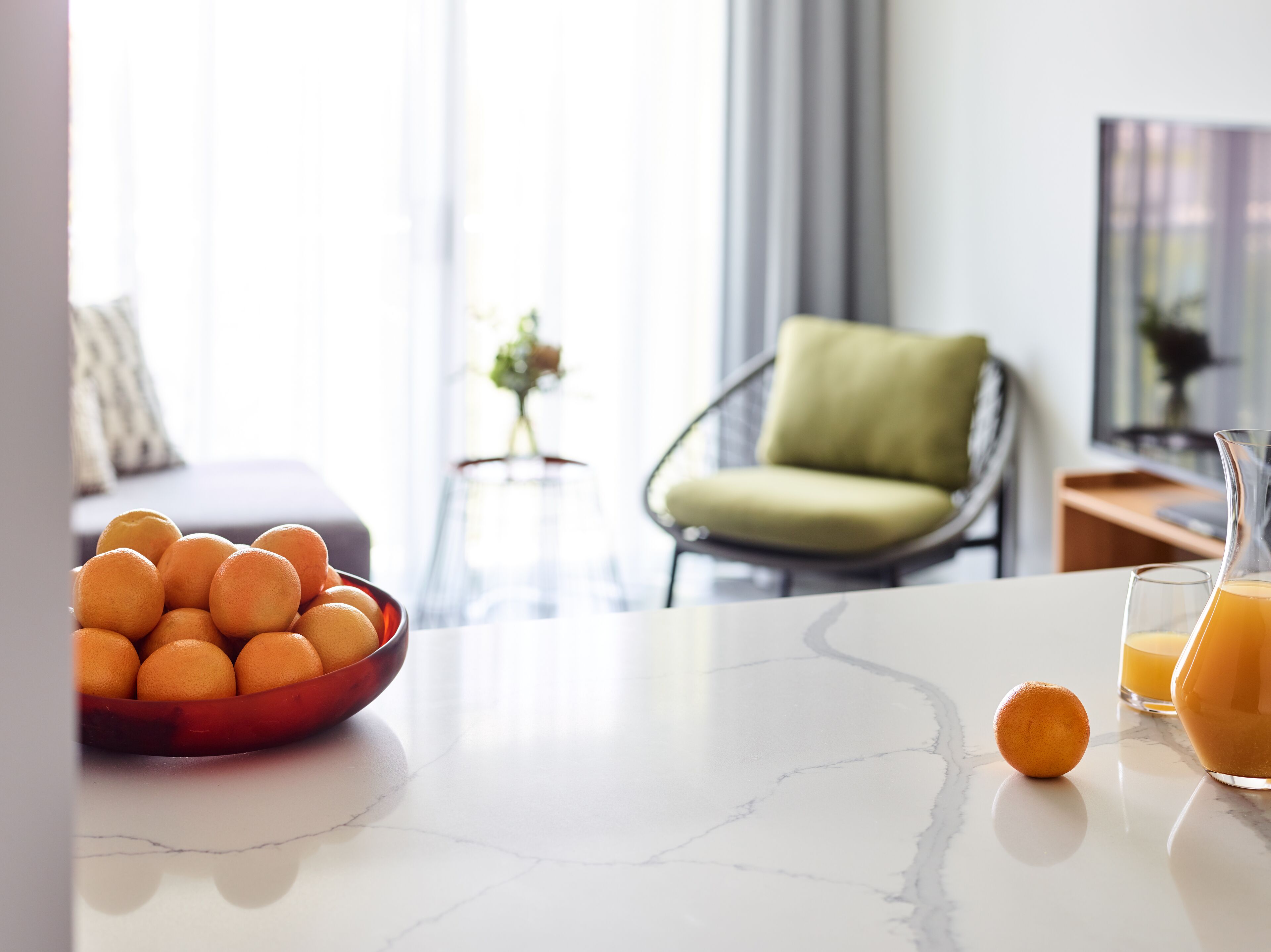 Un plan de travail de cuisine avec un bol d’oranges, un verre de jus d’orange et un dessus en marbre.