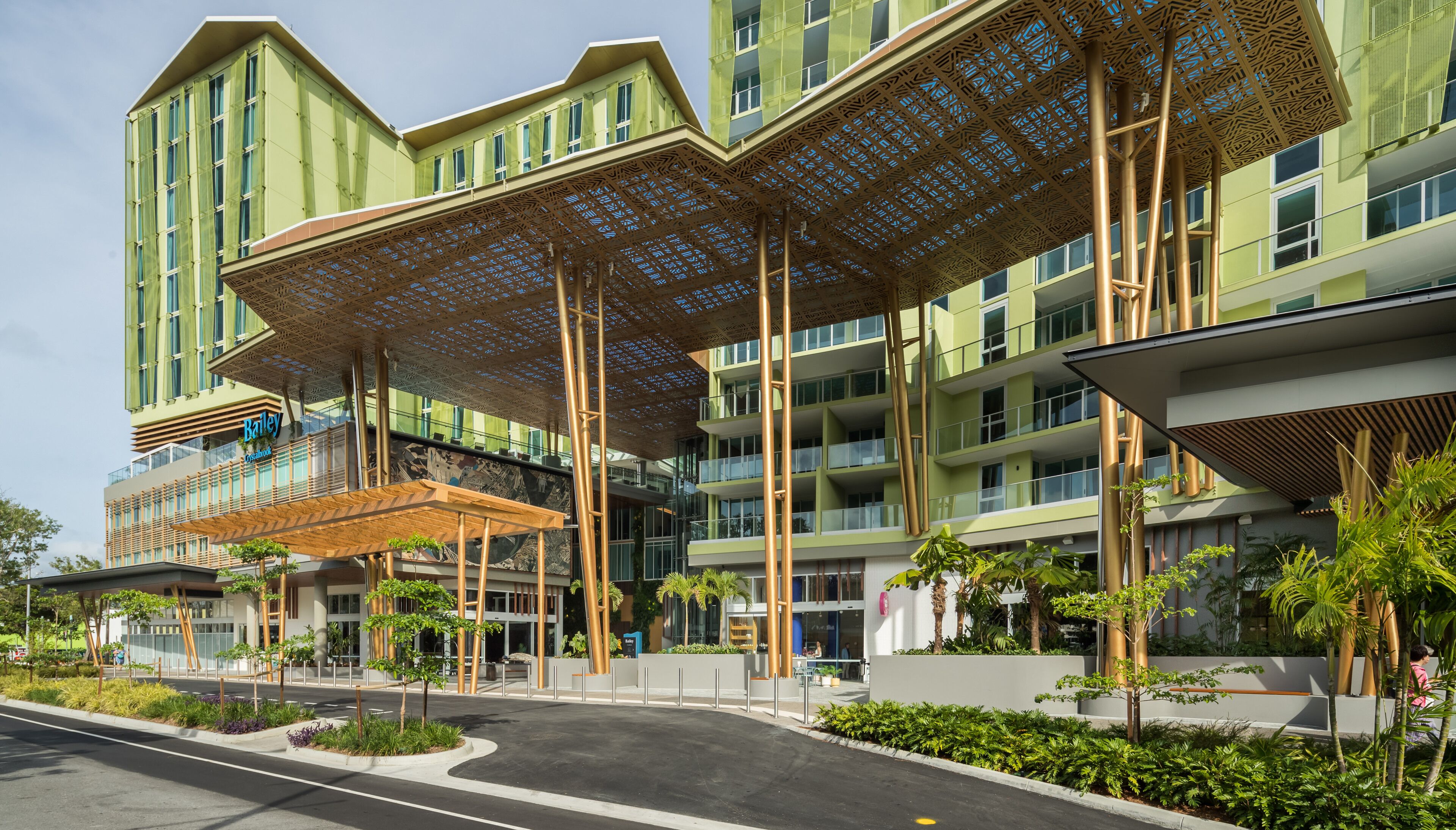 A modern hotel with a green facade, multiple balconies, and a covered outdoor area with plants.