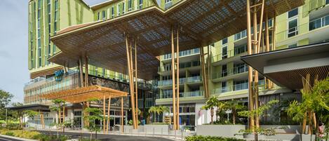 A modern hotel with a green facade, multiple balconies, and a covered outdoor area with plants.