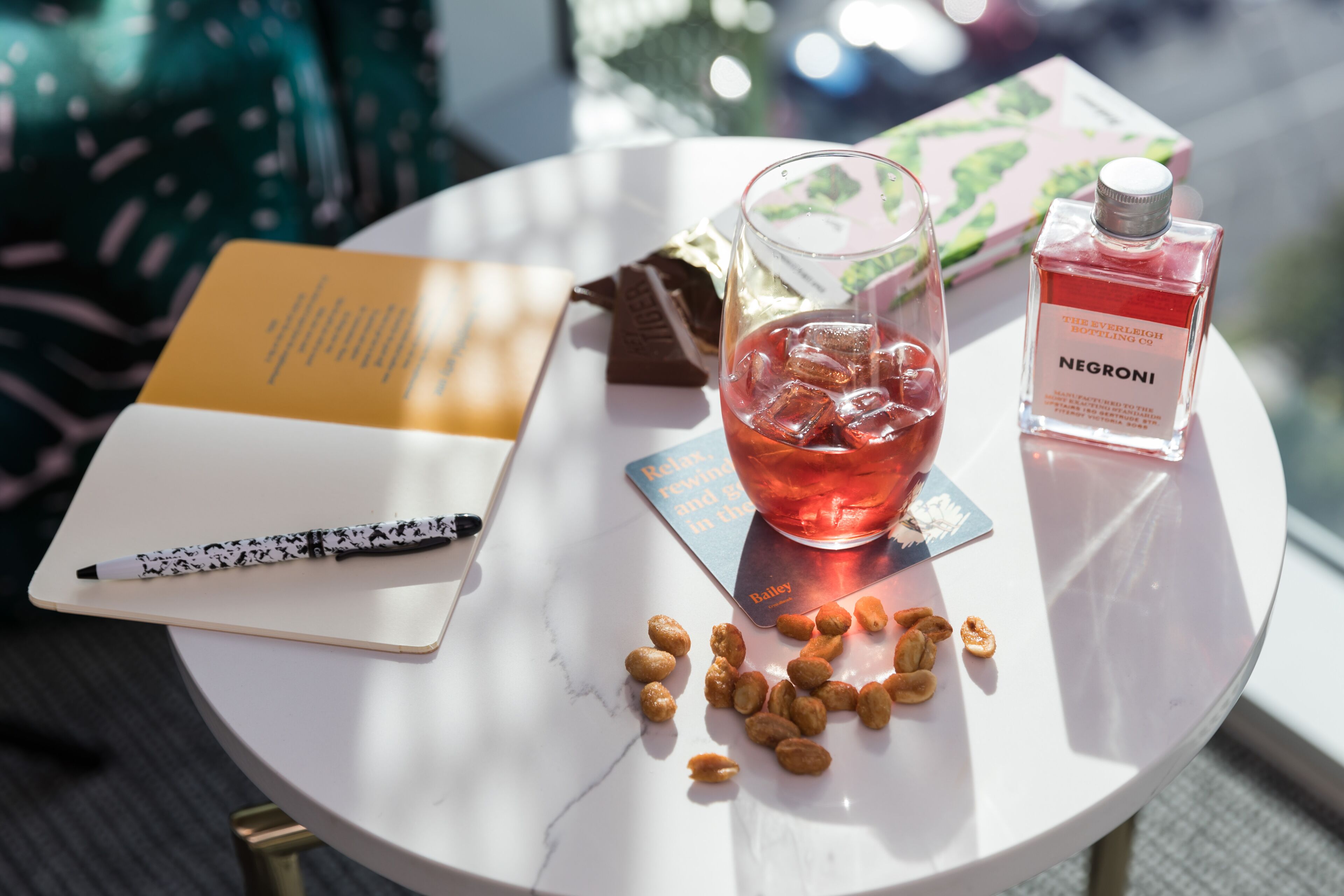 A table with a notebook, pen, glass of red drink, bottle of perfume, and scattered nuts.