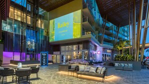A modern hotel lobby with a large digital screen displaying the name "Bailey," comfortable seating areas, and a well-lit atrium with a patterned ceiling. - Crystalbrook Bailey (Cairns)