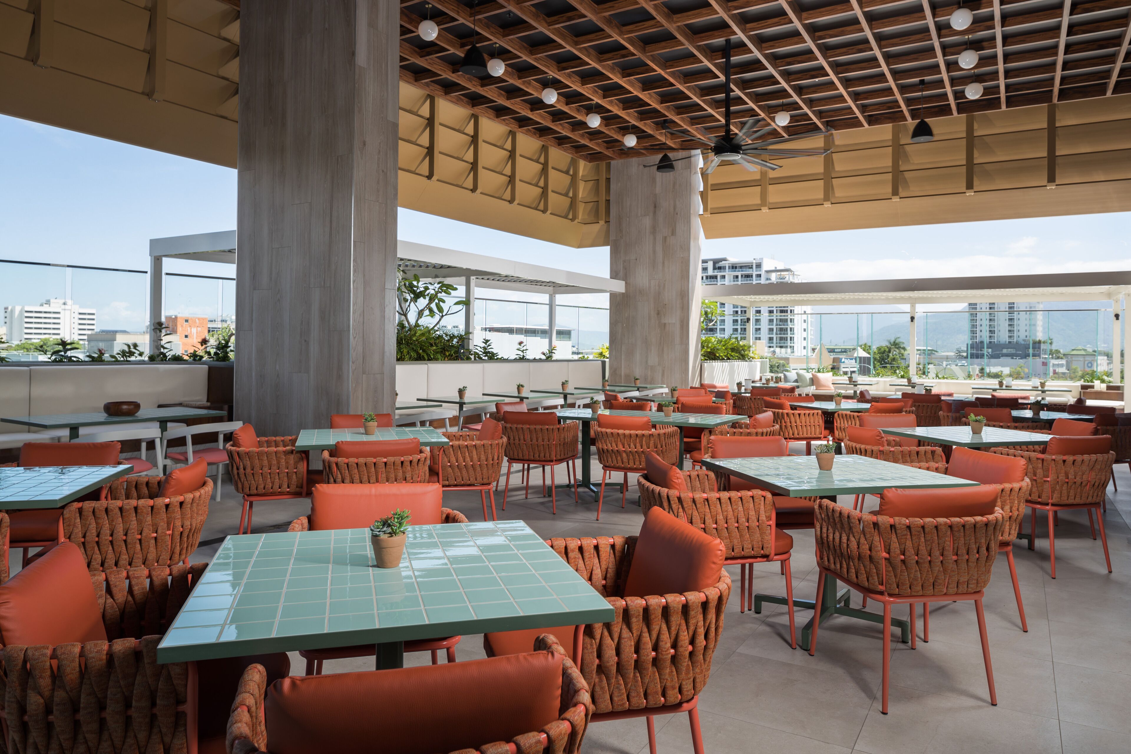 A rooftop dining area with multiple tables and chairs, large pillars, and a view of the cityscape.