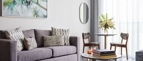 Un salón moderno con un sofá gris, cojines estampados, una mesa redonda de centro con libros y un jarrón floral.