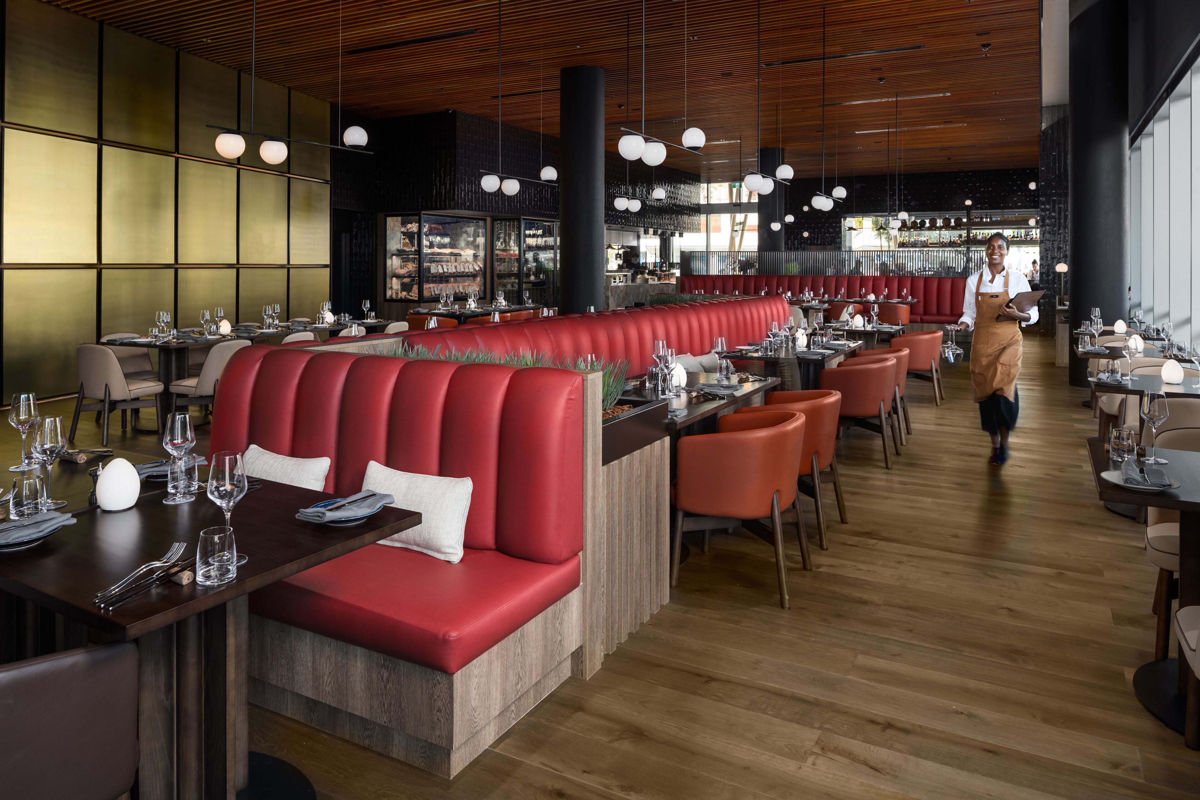 Un restaurante moderno con asientos rojos, piso de madera e iluminación colgante.