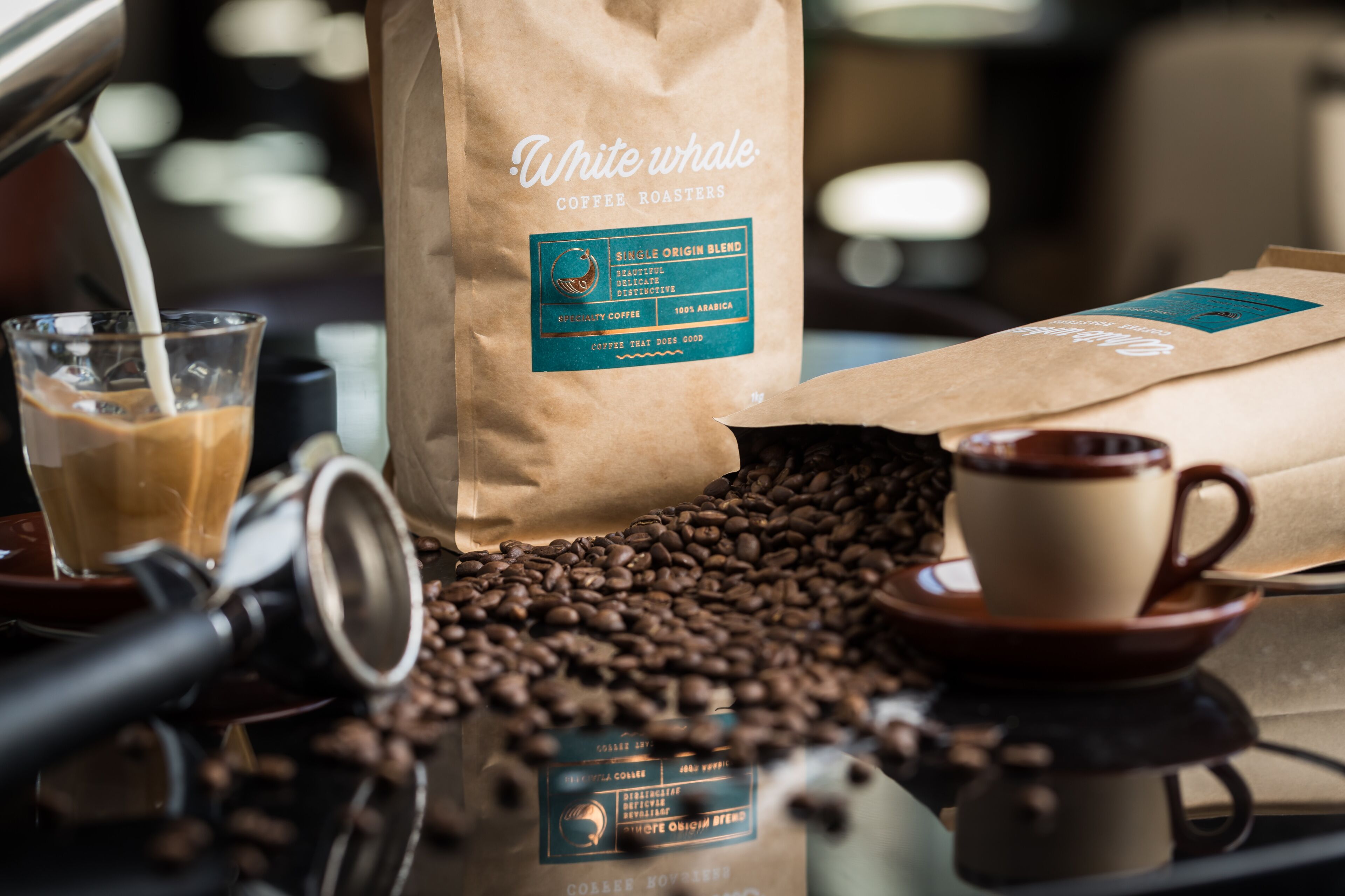 A coffee machine, a glass of iced coffee, a bag of coffee beans, and a cup of coffee on a table.