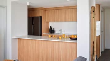 A modern kitchen with wooden cabinets, a black refrigerator, and a white countertop with a bowl of oranges.
