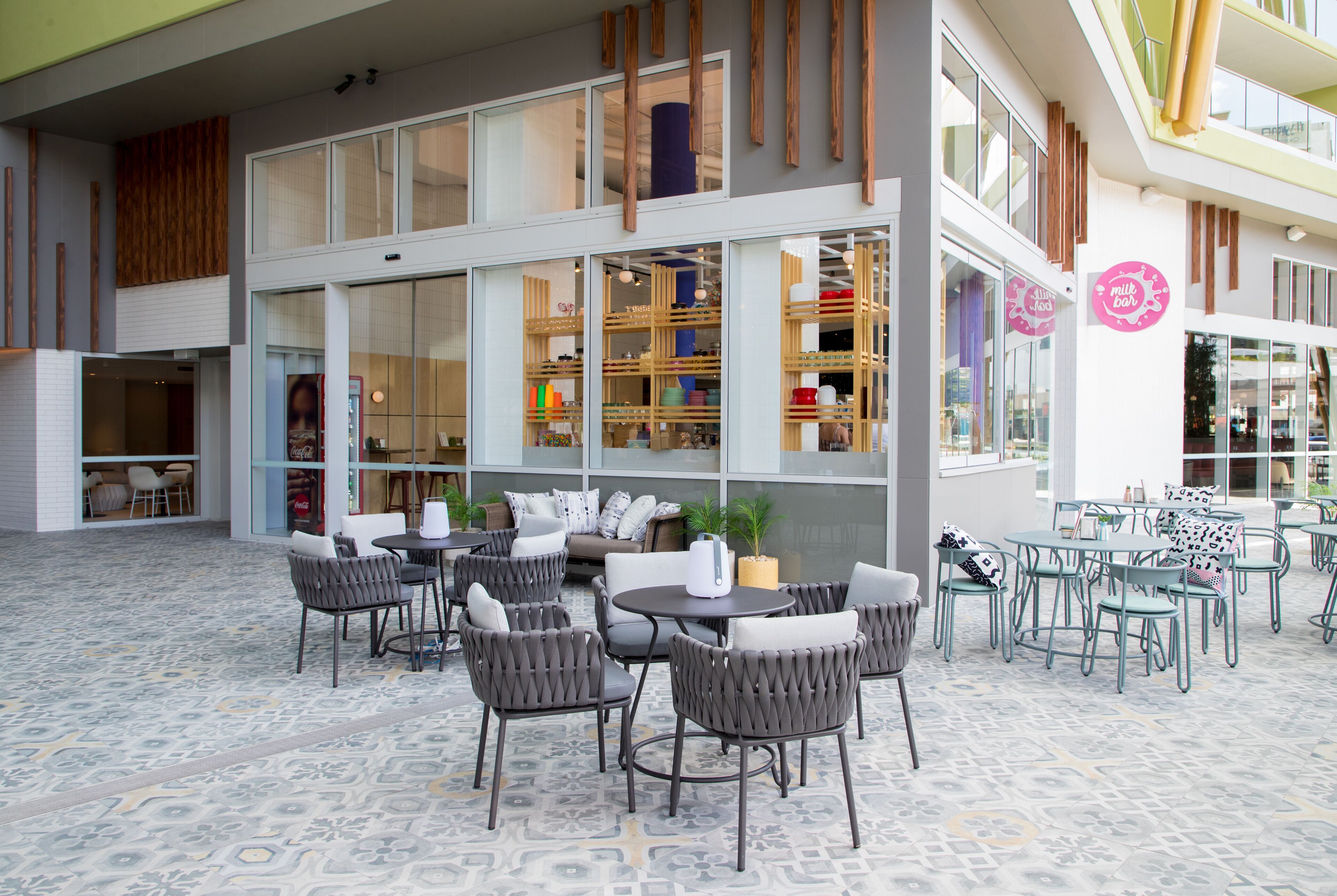 An outdoor seating area with wicker chairs and tables, a patterned floor, and a view of the interior through large windows.