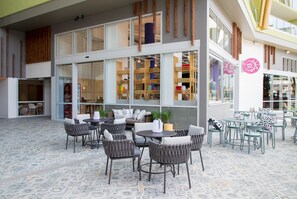 An outdoor seating area with wicker chairs and tables, a patterned floor, and a view of the interior through large windows. - Crystalbrook Bailey (Cairns)