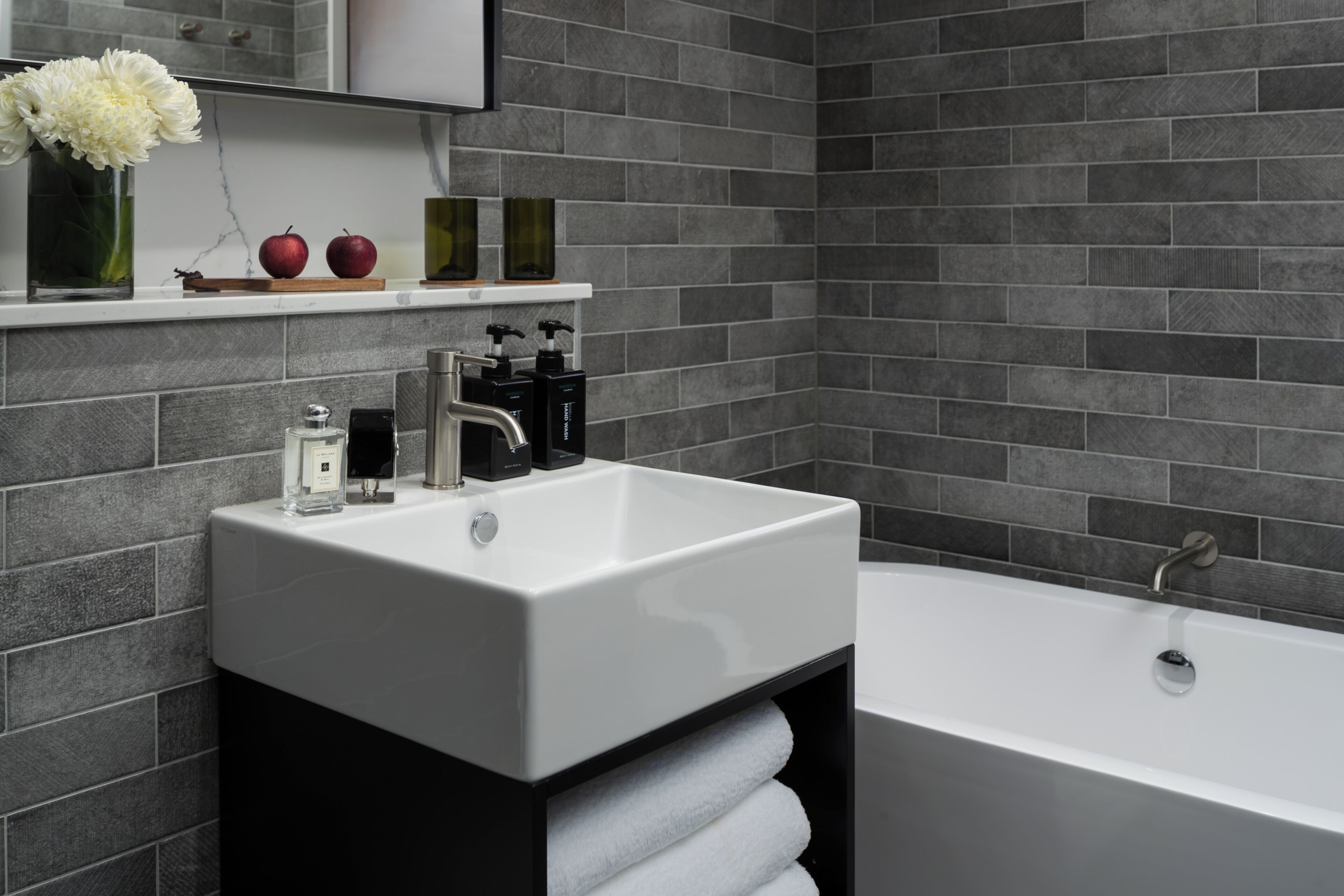 A modern bathroom with a white sink, black cabinet, and a bathtub.