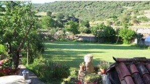 Entorn rural a l'aire lliure amb una taula de pedra i plantes en testos, envoltat de verdura i una vista a un paisatge llunyà.
