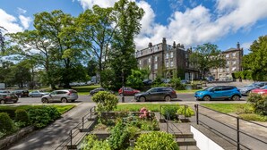 A residential street with parked cars, a row of houses, and a well-maintained garden area.